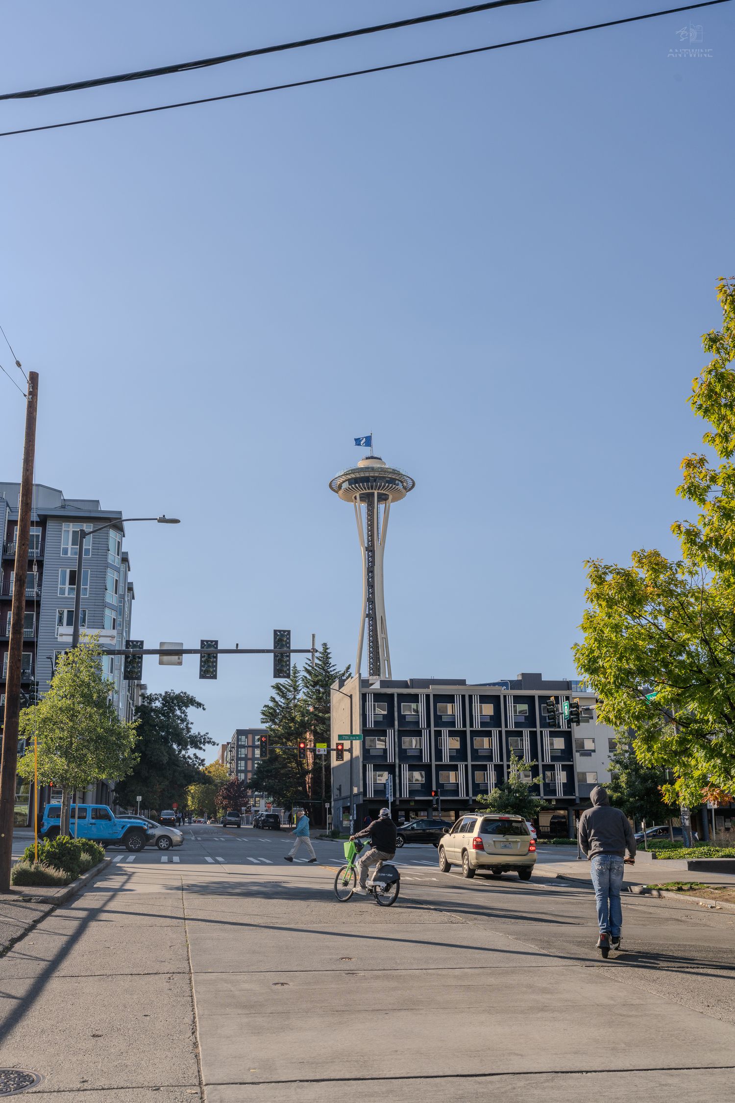 Seattle Space Needle tower visible from a busy street intersection with cyclists and cars below.