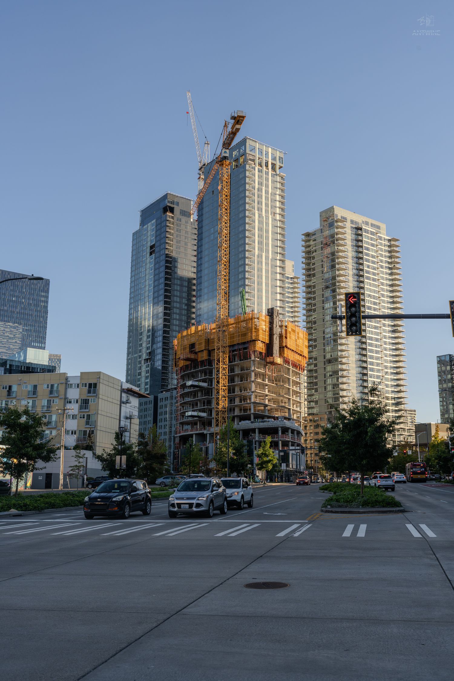 Urban construction site with cranes and skyscrapers at a city intersection under clear sky.