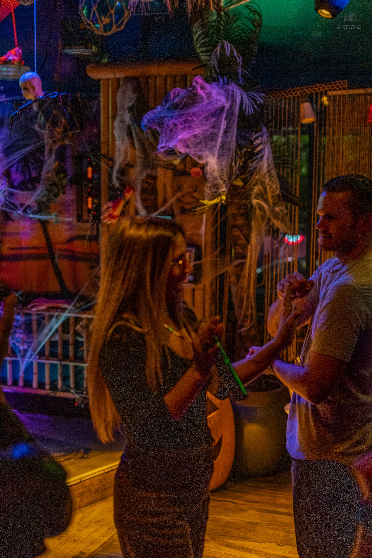 Couple dancing at a Halloween-themed karaoke bar with spooky decorations and colorful neon lights.