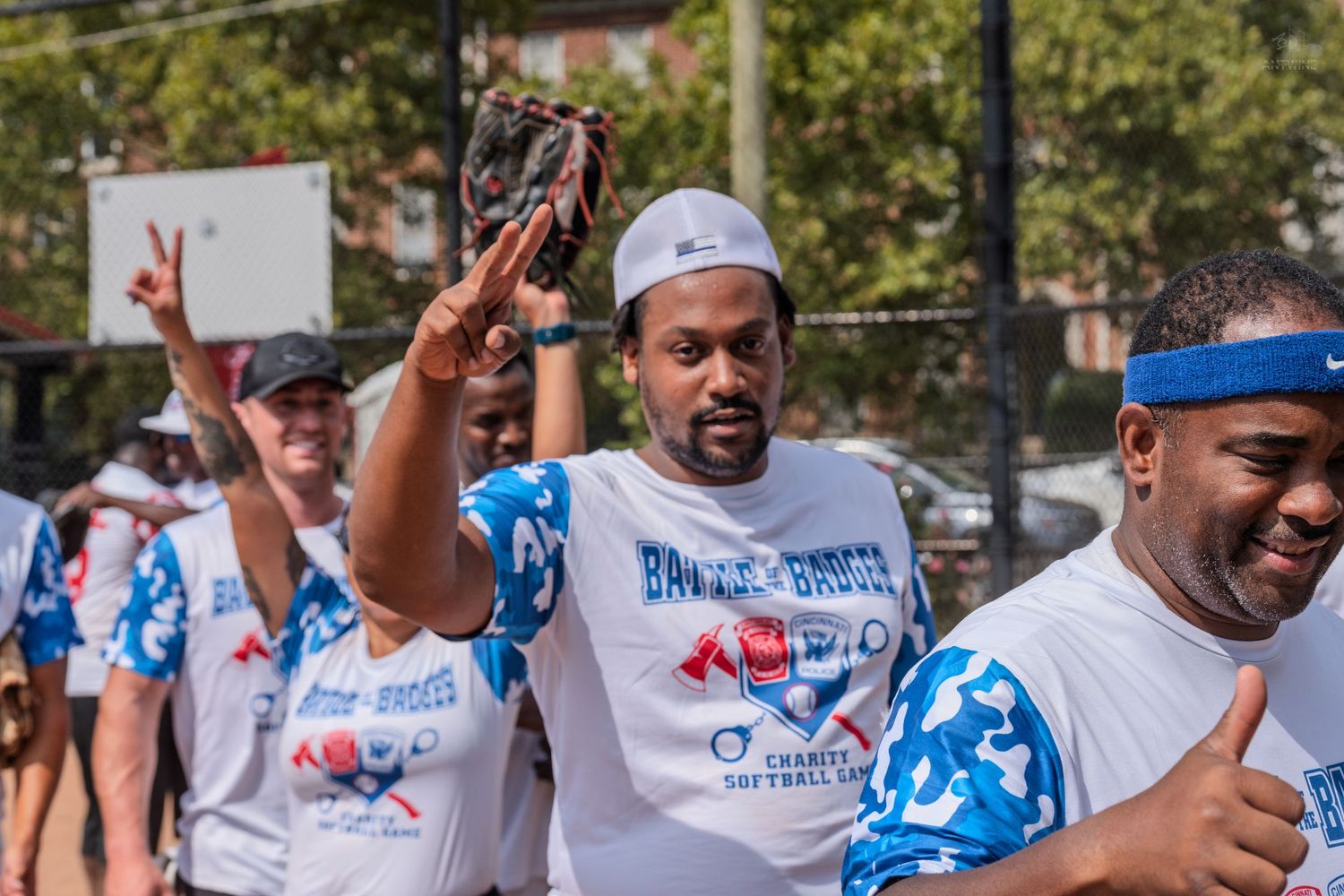 Smiling player in Battle of the Boroughs charity softball jersey holds up peace sign while wearing a baseball glove.