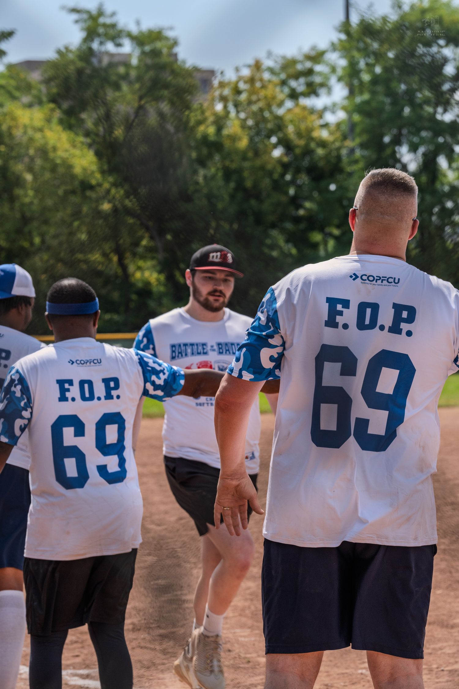FOP softball team players exchange high fives on baseball diamond during outdoor charity game.