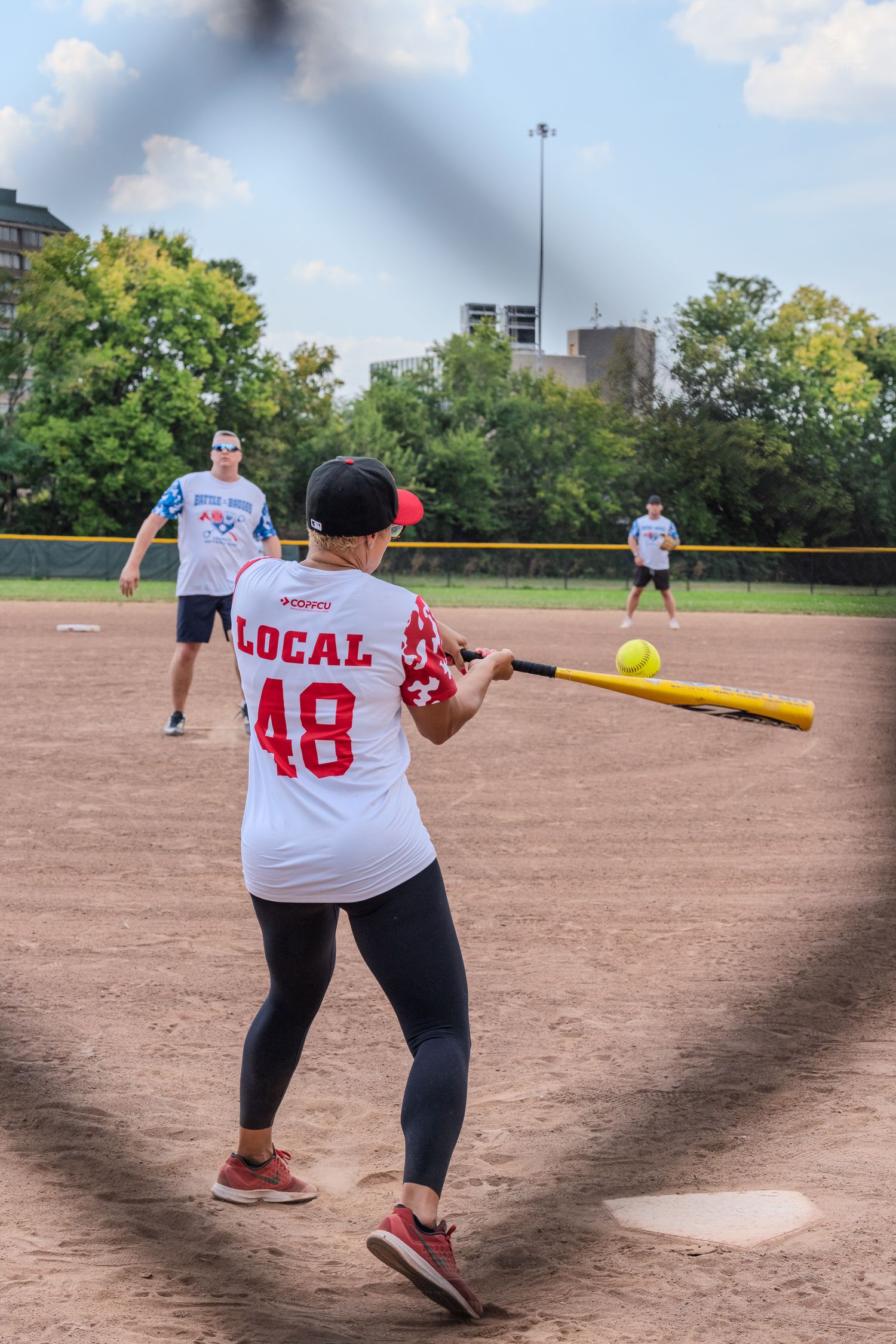 Player number 48 in Local jersey swinging at a yellow softball during a charity game.