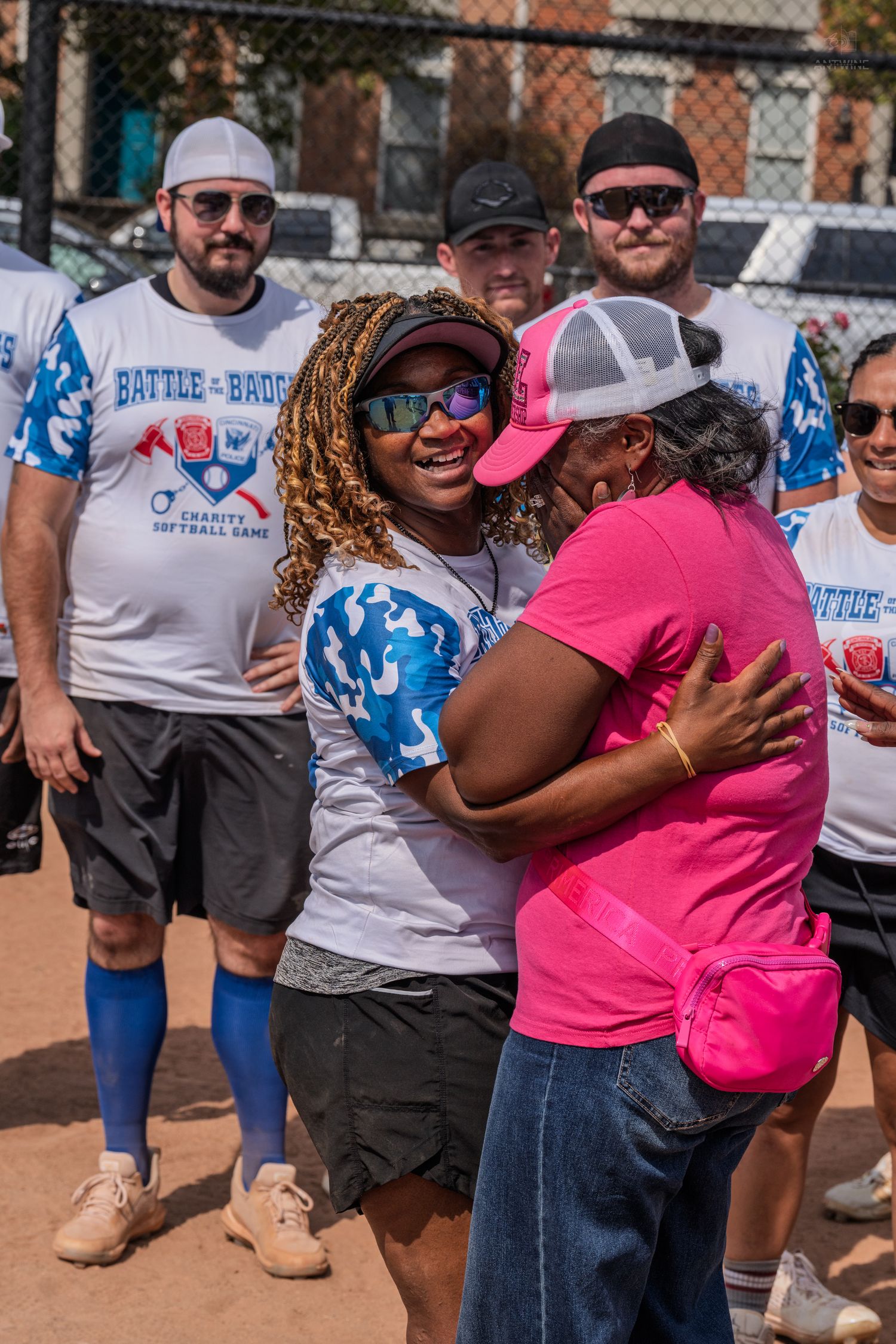 Player in Battle of the Badges charity softball jersey shares warm hug with woman in pink.