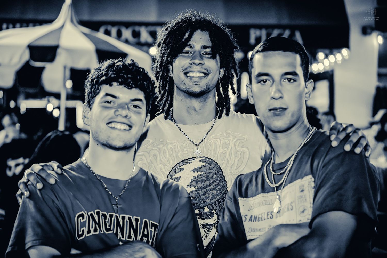 Three young men posing together smiling at an outdoor festival.