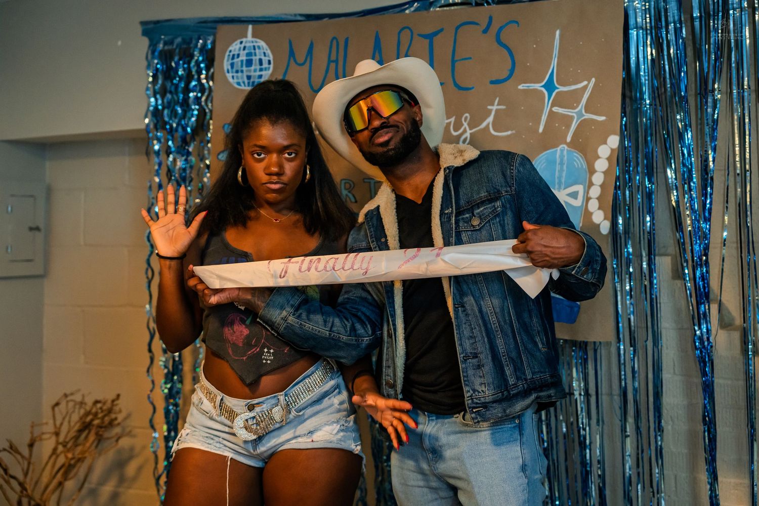 Couple poses with a decorative banner at a blue-themed birthday celebration.