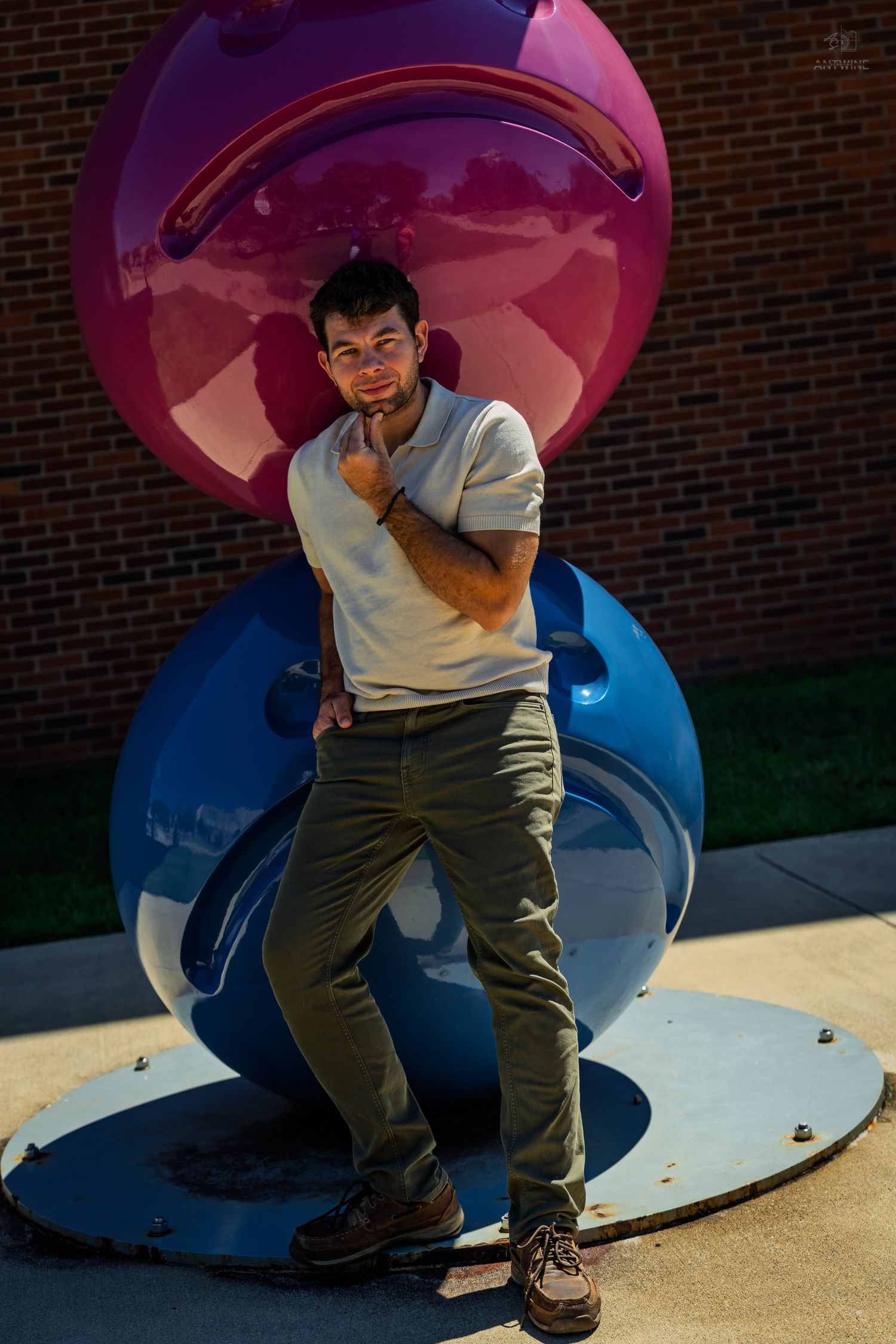 Man in white polo posing confidently beside large purple and blue spherical sculpture outdoors.