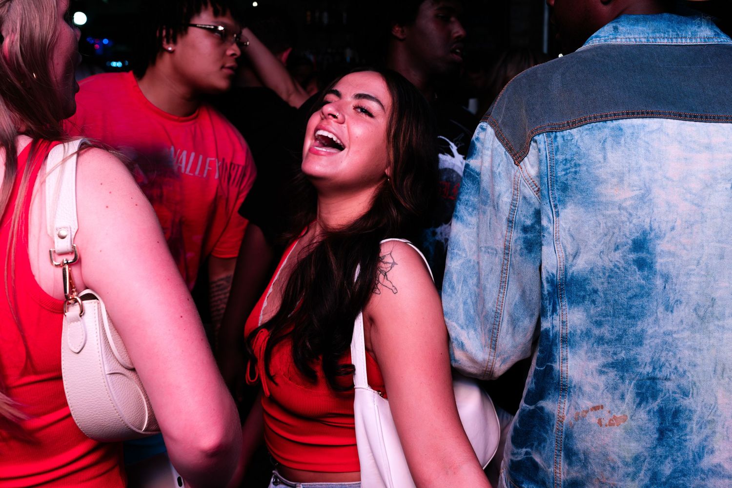 Young woman laughing joyfully at a crowded nightclub event wearing a red top.