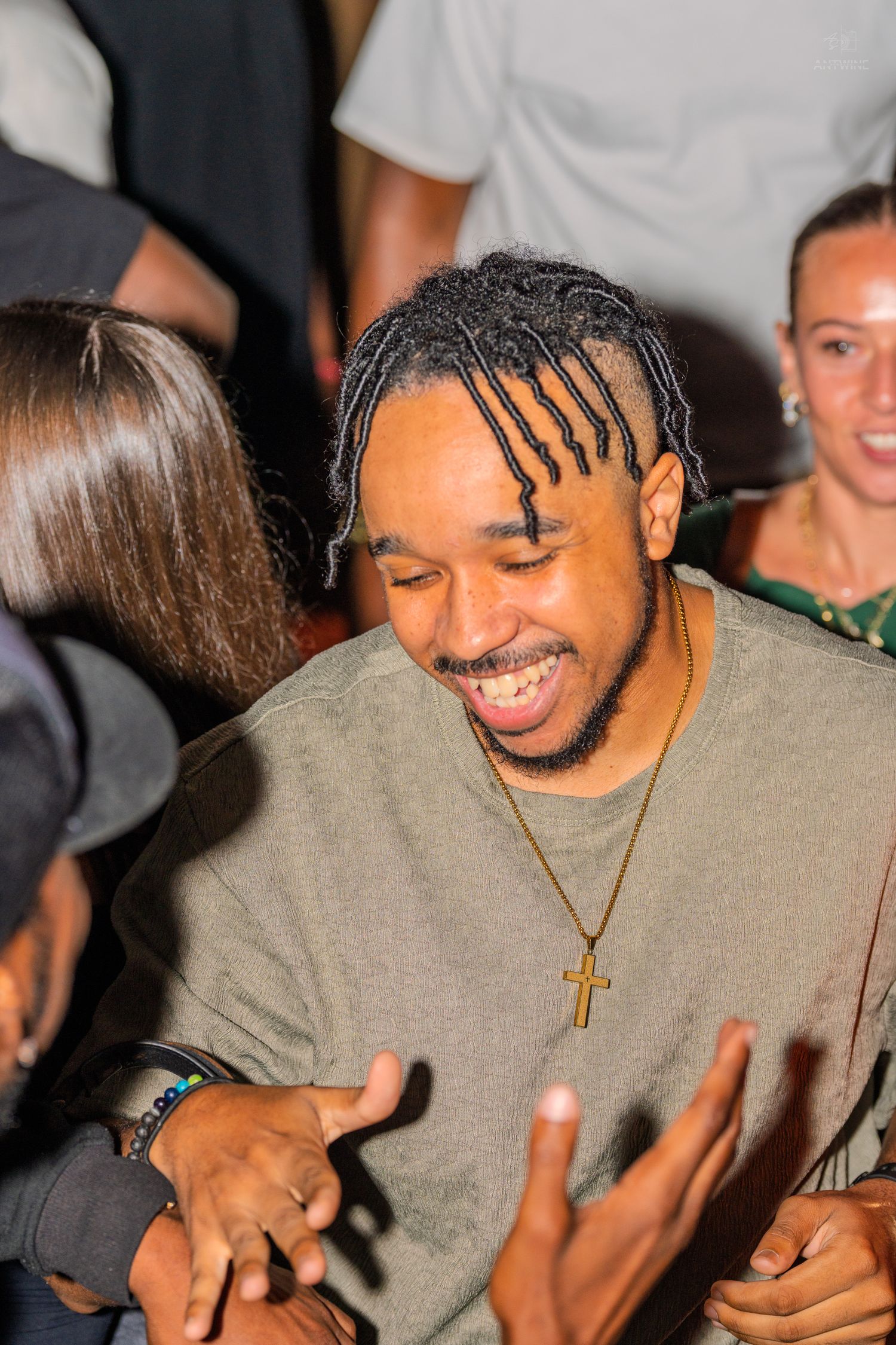 Smiling young man with braided hair and gold cross necklace dancing at a lively party.