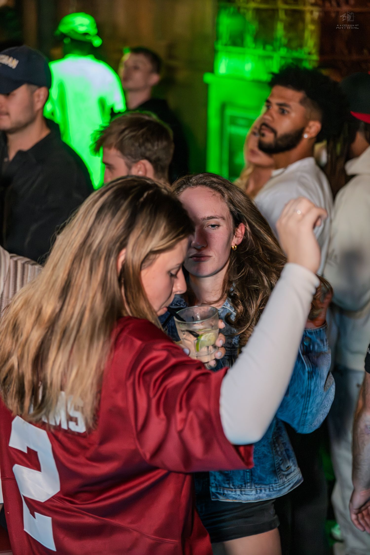 Two young women dancing together at a crowded nightclub with green neon lights.