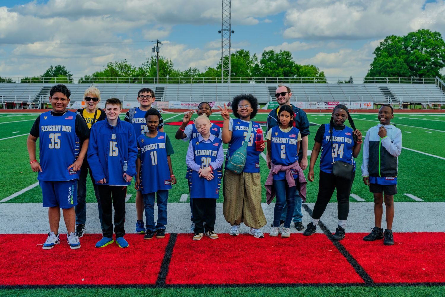 Group of kids in blue Pleasant View jerseys posing on a red carpet on a football field.