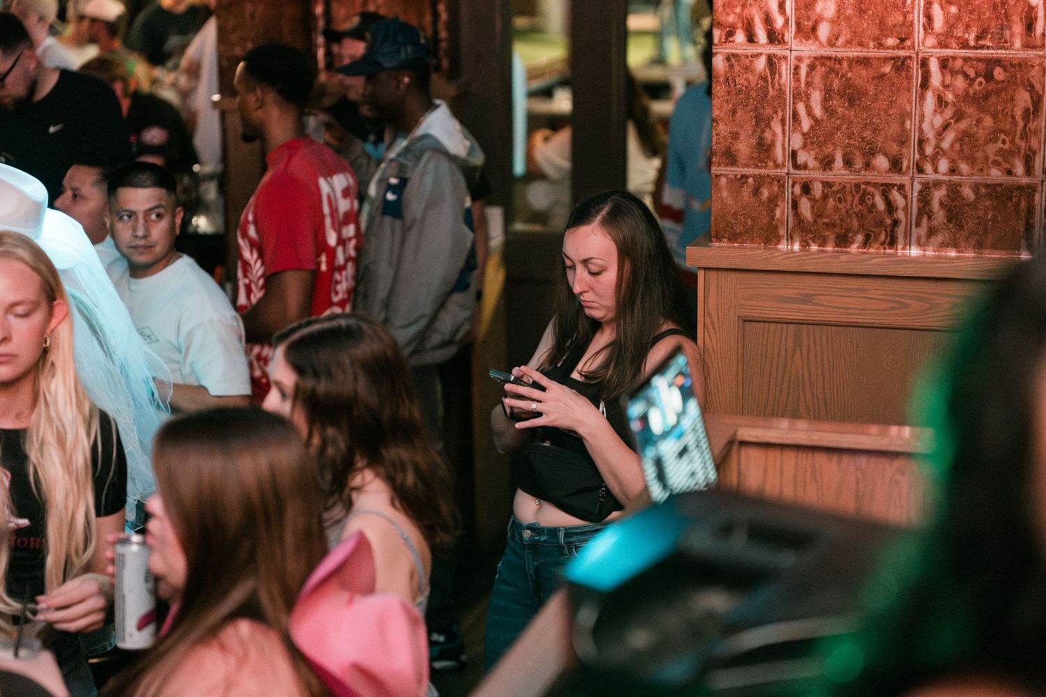Young woman checking her phone at a busy bar surrounded by a lively crowd.