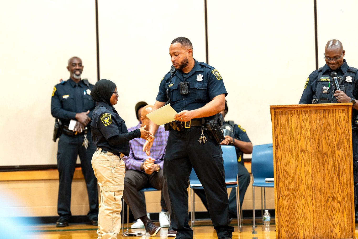 Police officers presenting a certificate to a young child during a law enforcement community event in a meeting hall.
