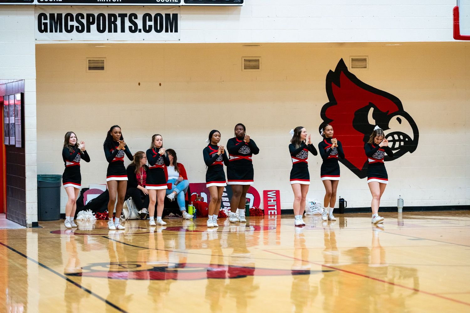 Basketball players compete on the court as a teammate signals from the background during a high school game.