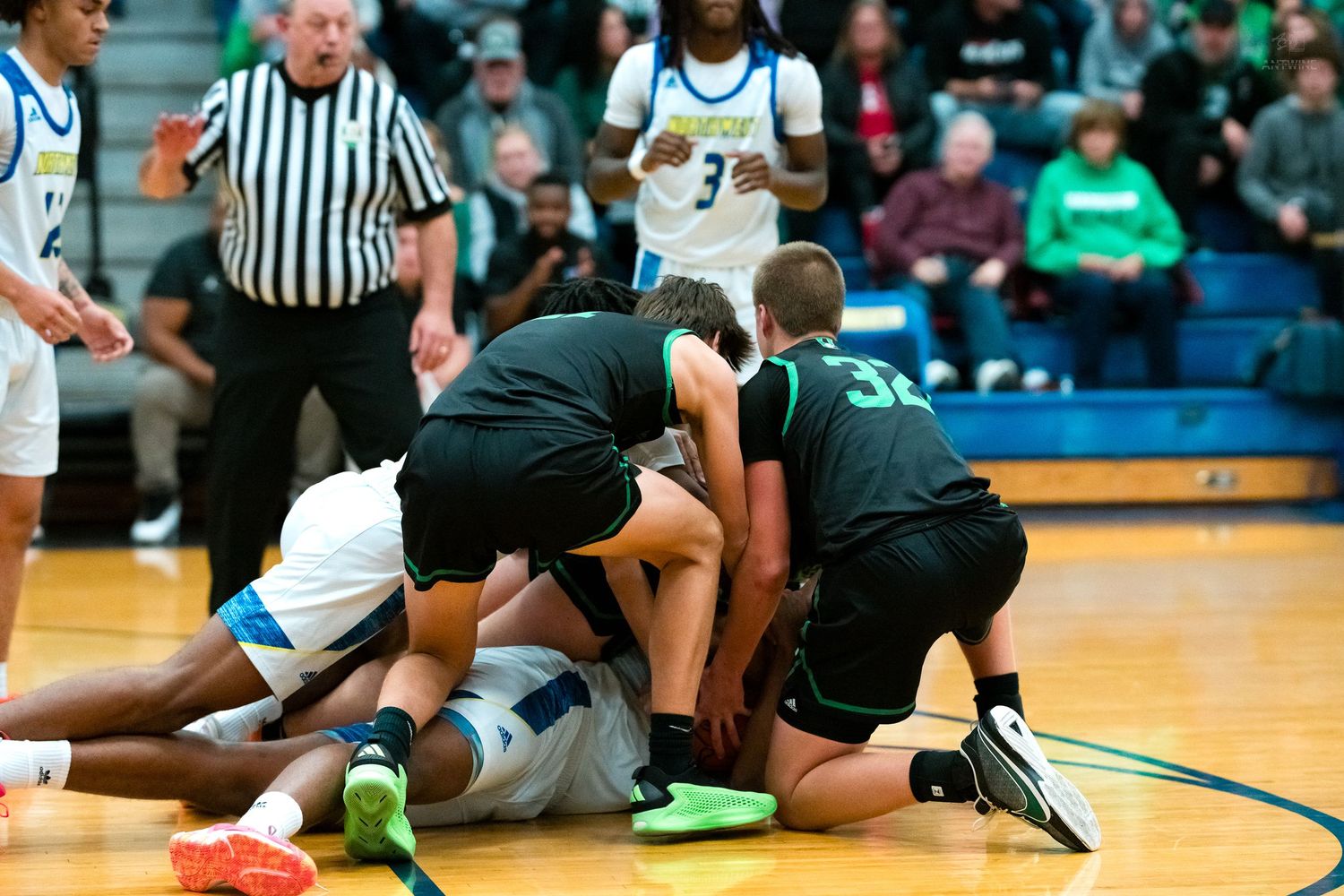 Multiple players scramble for loose ball on basketball court during intense game.