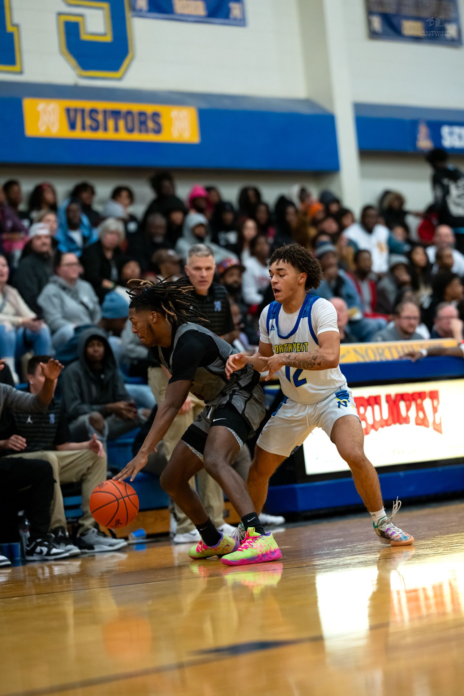 Basketball player in white uniform defends against opponent dribbling during an intense high school game.