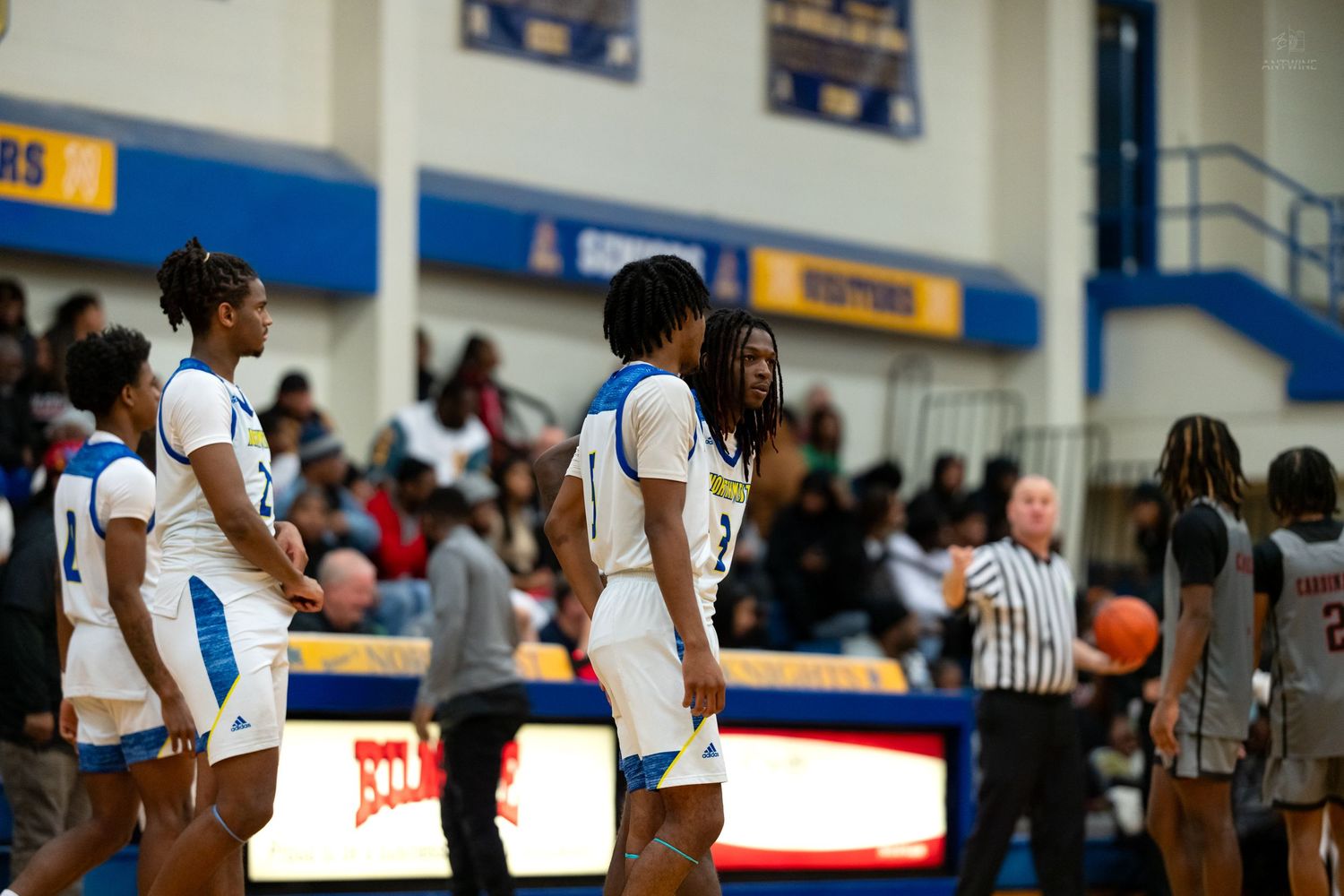 High school basketball players in blue uniforms huddle together on court during indoor game.