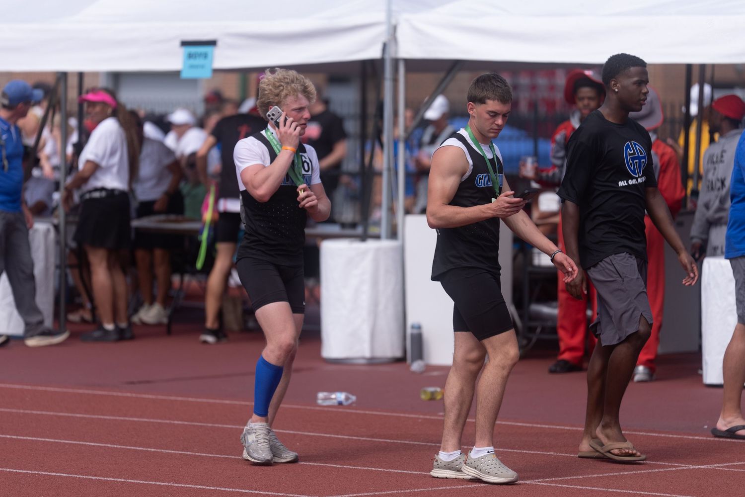 Athletes in track uniforms walk along the sidelines at an outdoor track and field competition.
