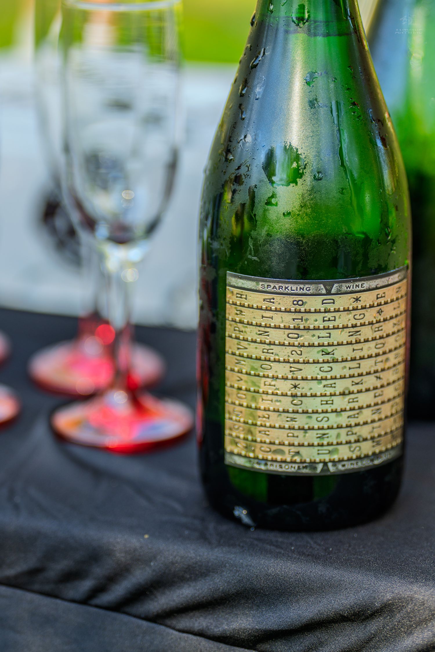 Chilled green sparkling wine bottle with vintage label beside champagne flutes on black tablecloth.