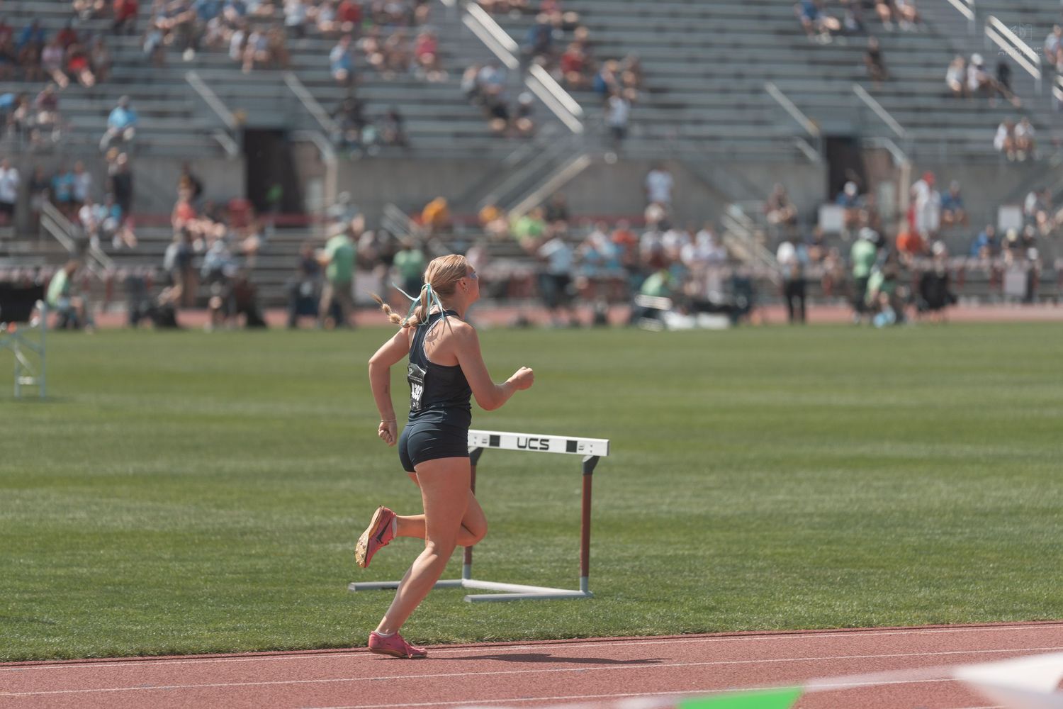 Female athlete clearing hurdle on red track at outdoor collegiate track and field meet.