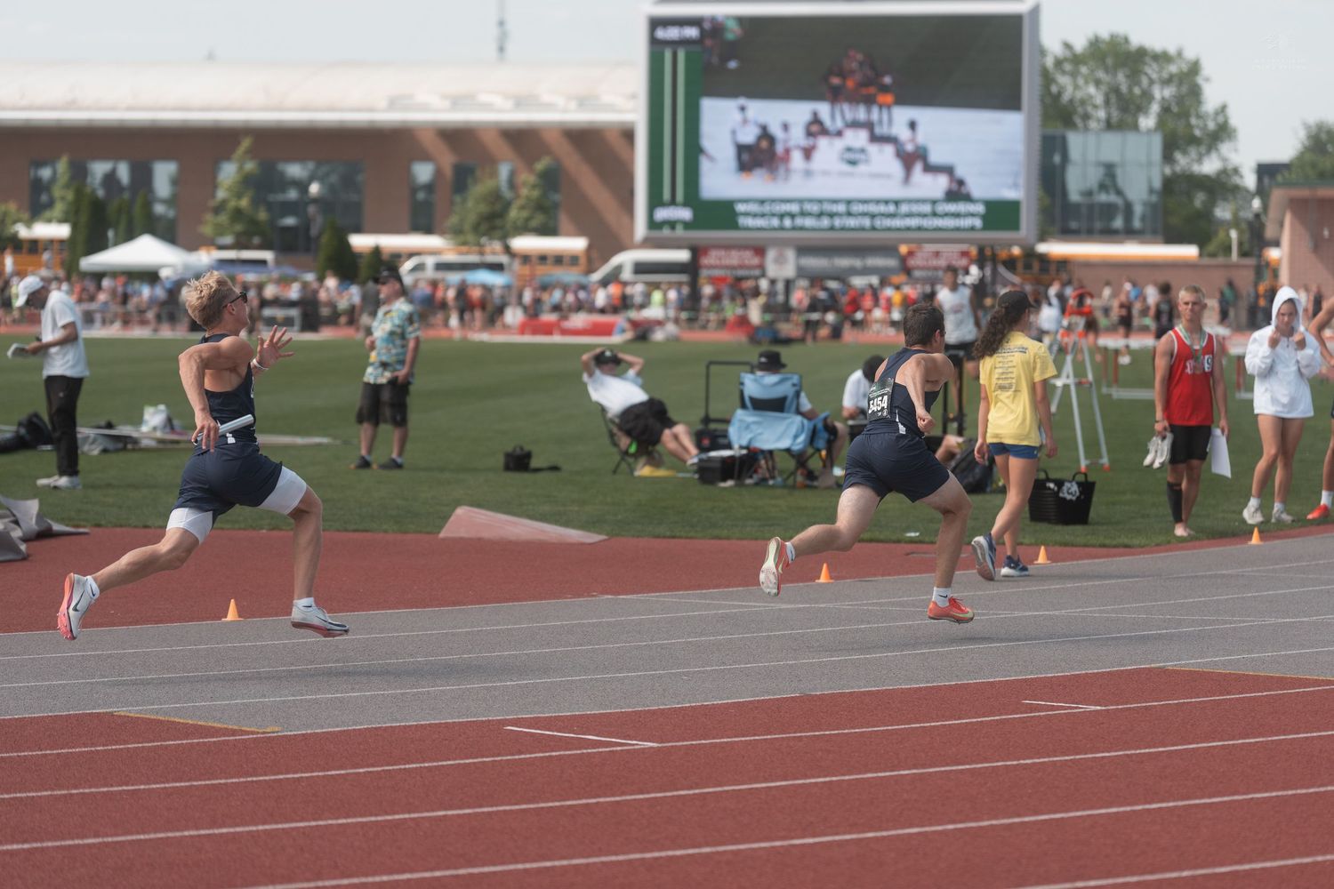 Female athletes compete in sprint race on red track at outdoor track and field meet.