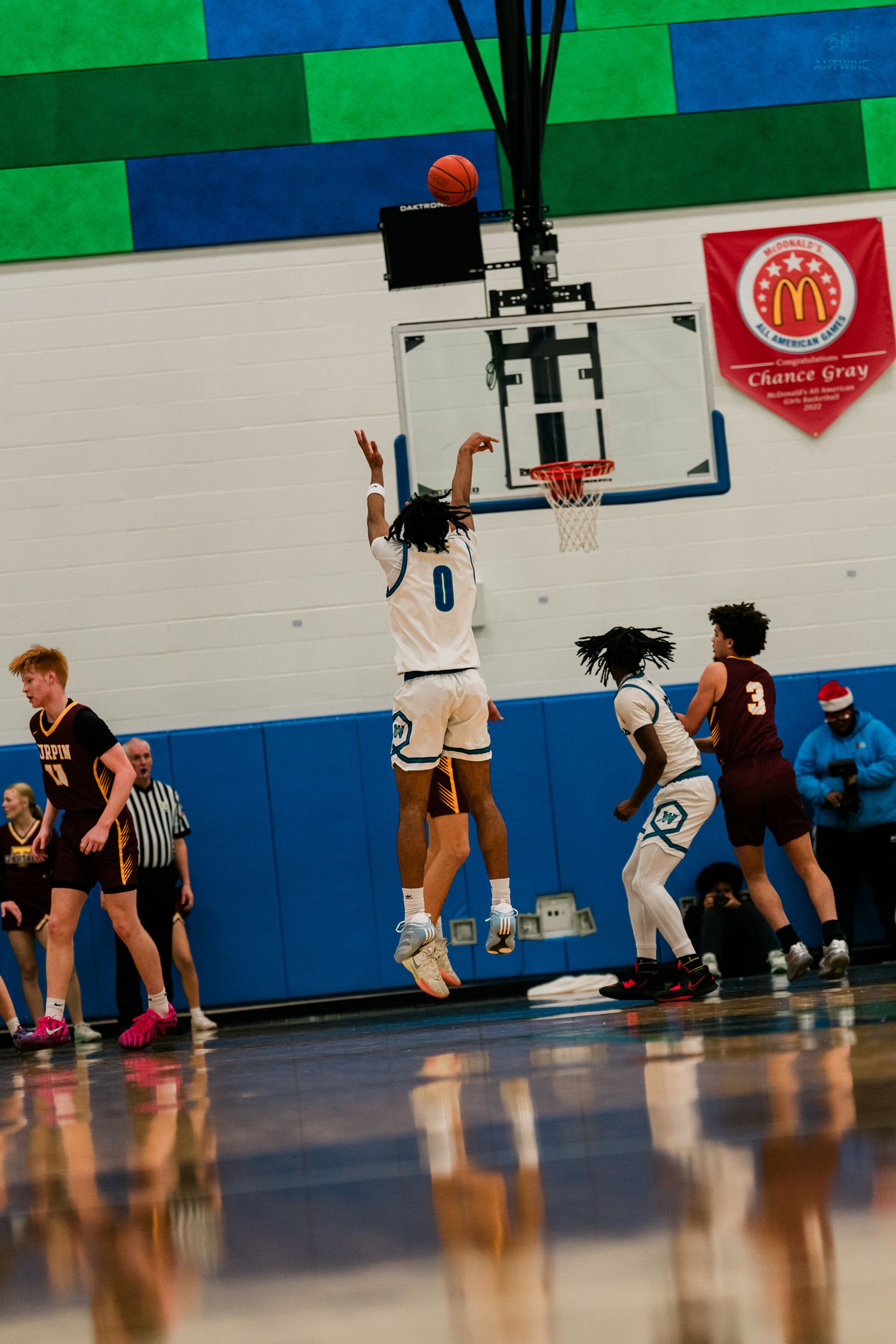 Basketball player in white number 0 jersey leaps for a shot near the hoop during high school game.