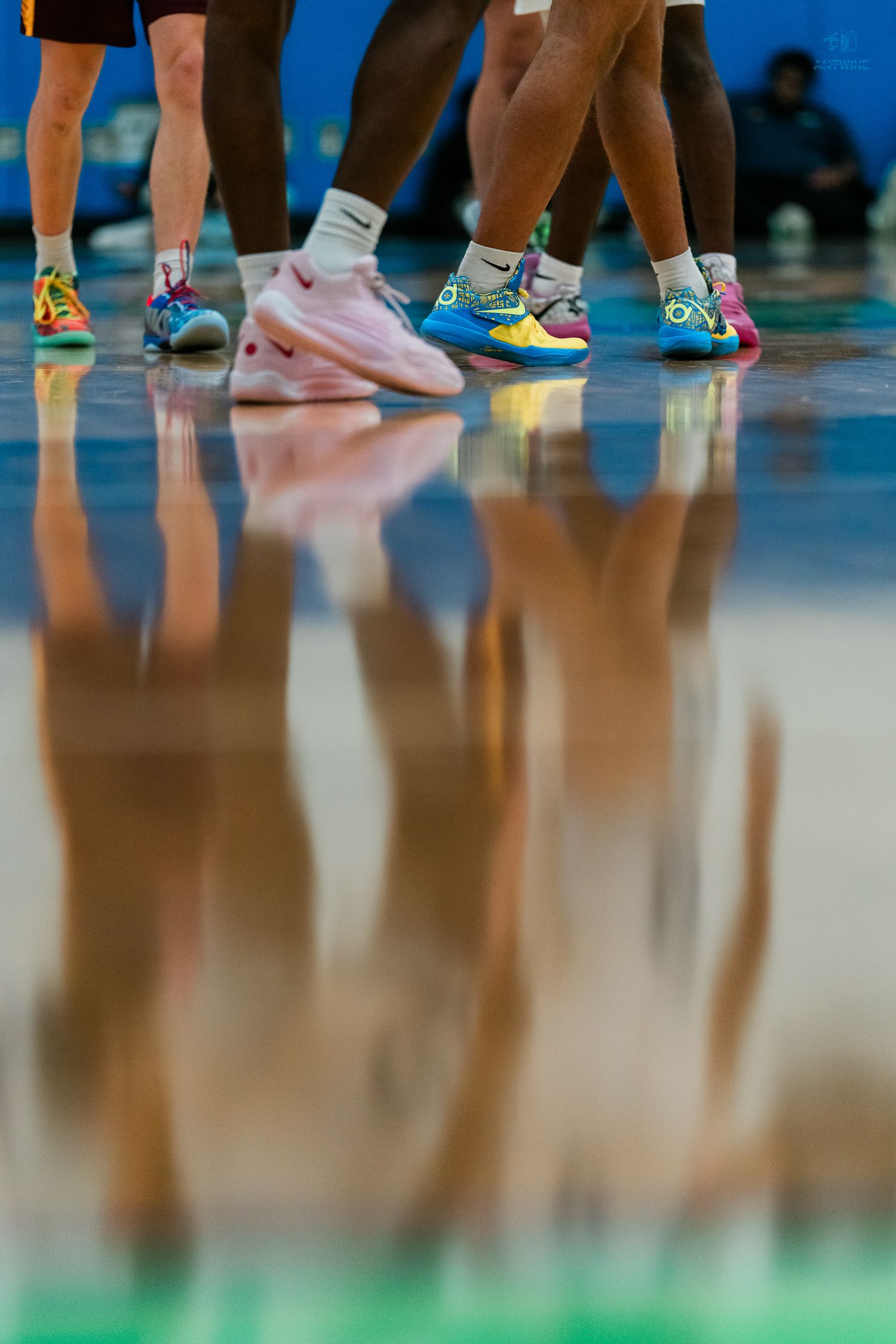 Colorful basketball sneakers reflect on a shiny hardwood court during a basketball game.