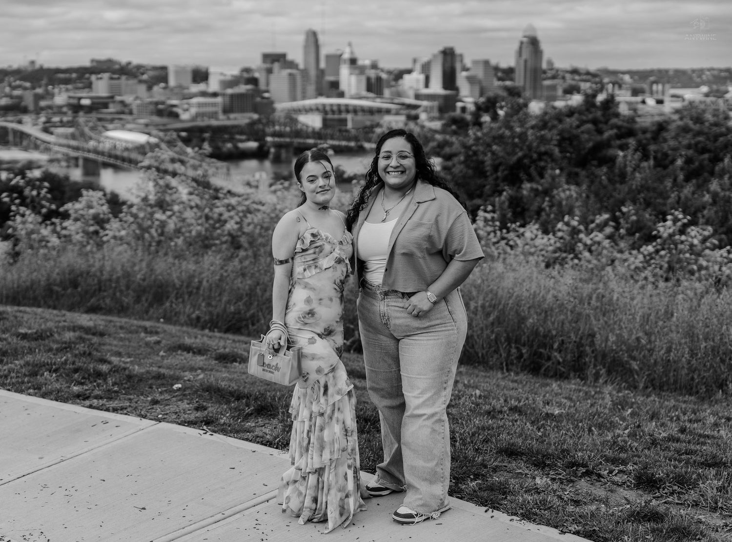 Two women smiling together on a hilltop overlook with Cincinnati skyline in black and white.