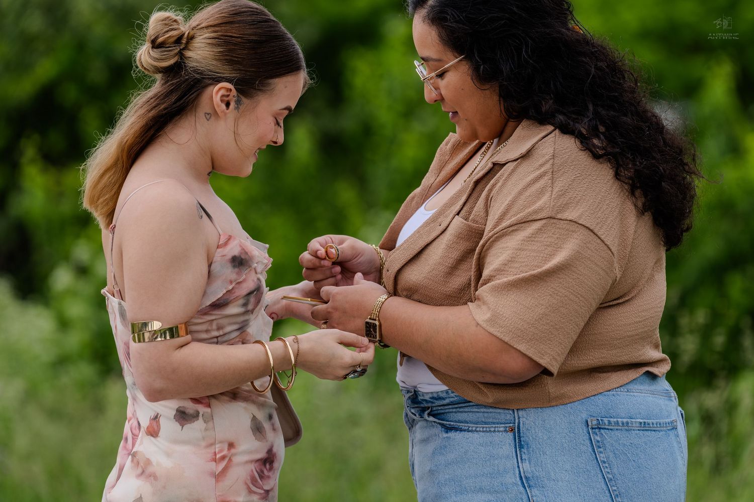 Close-up of two women examining an engagement ring outdoors surrounded by lush green foliage.