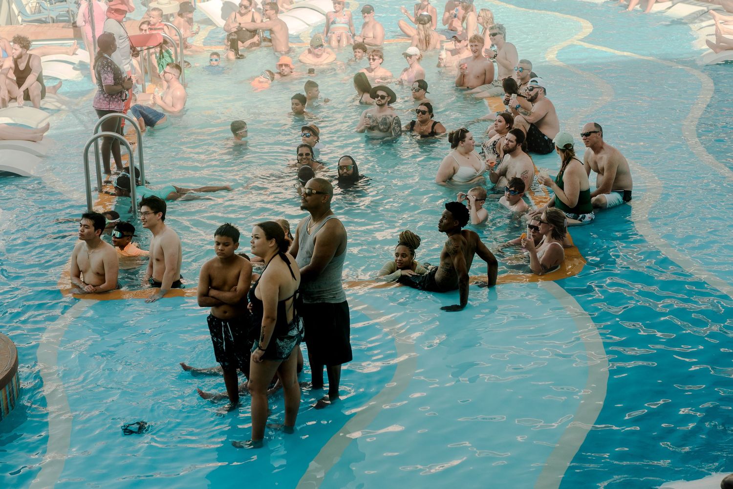 Crowds of people enjoying a busy resort swimming pool on a sunny day.