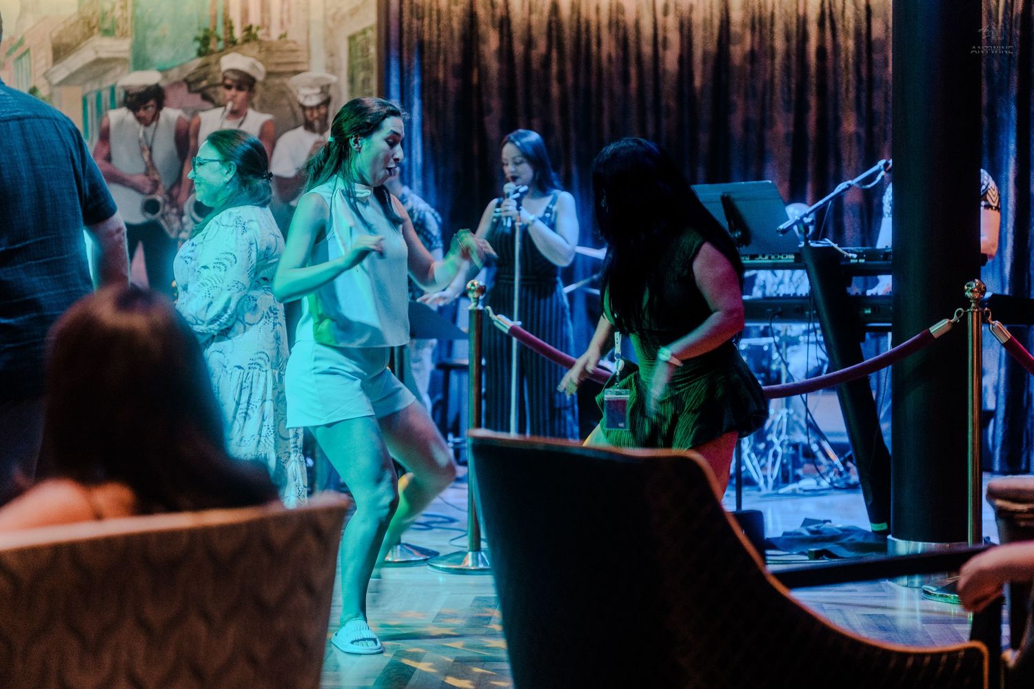 Live band and female vocalists performing on a cruise ship stage with teal lighting.