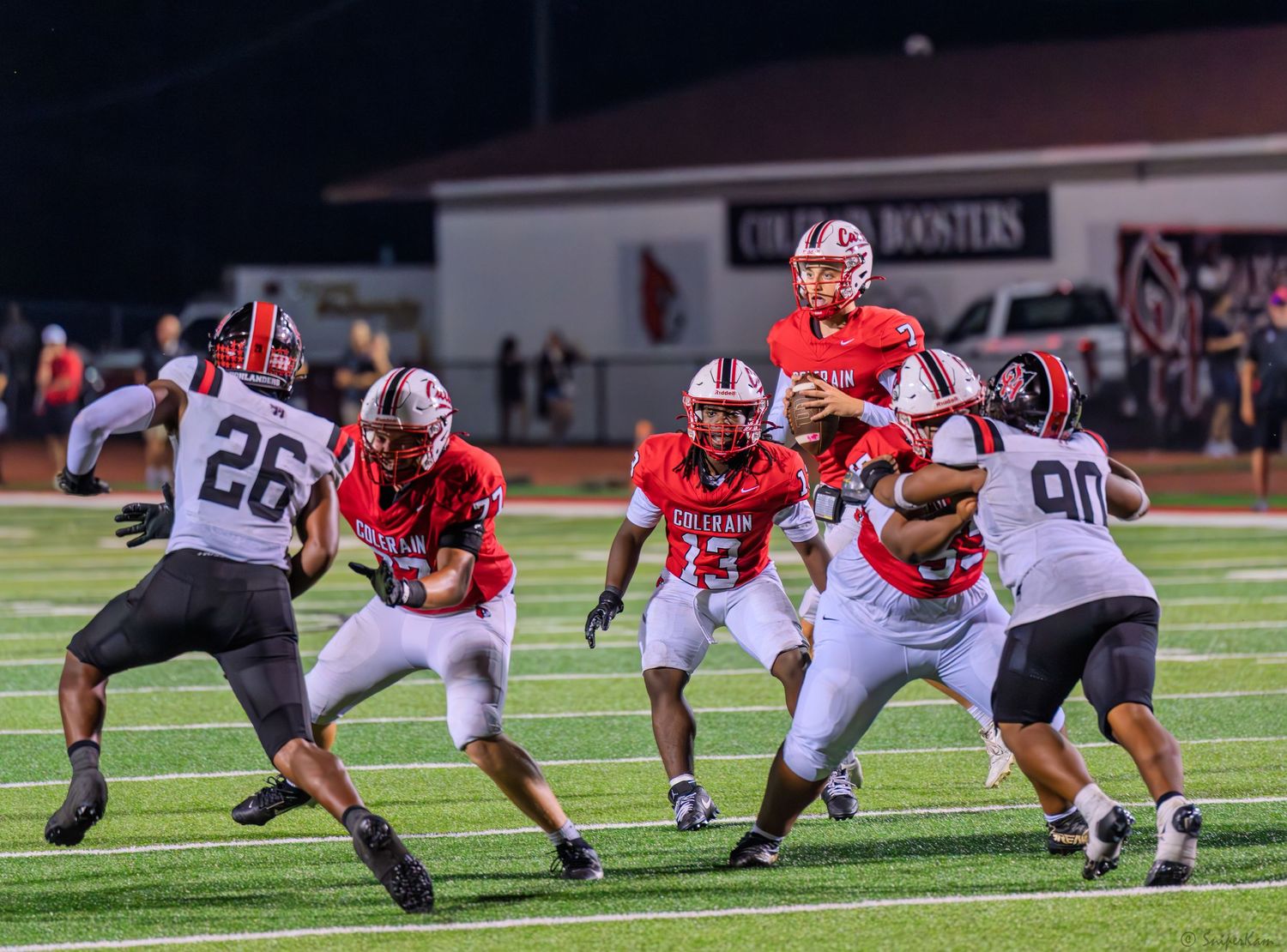 Colerain Cardinals quarterback scrambles behind blockers during a competitive high school football game.
