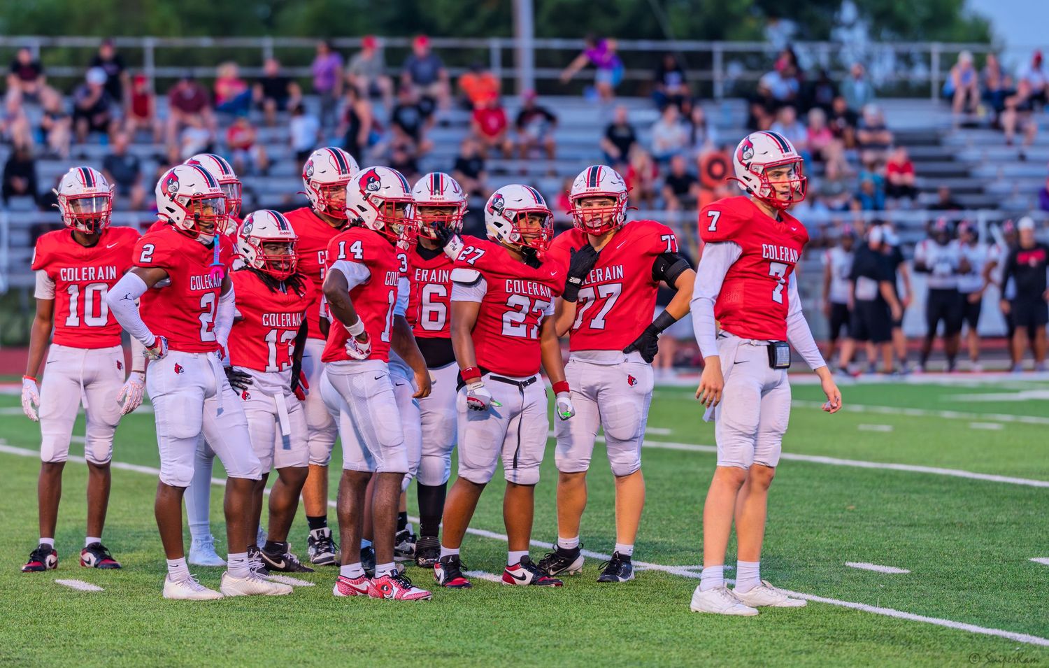 Colerain Cardinals football team huddles on the field in red home uniforms during a game.