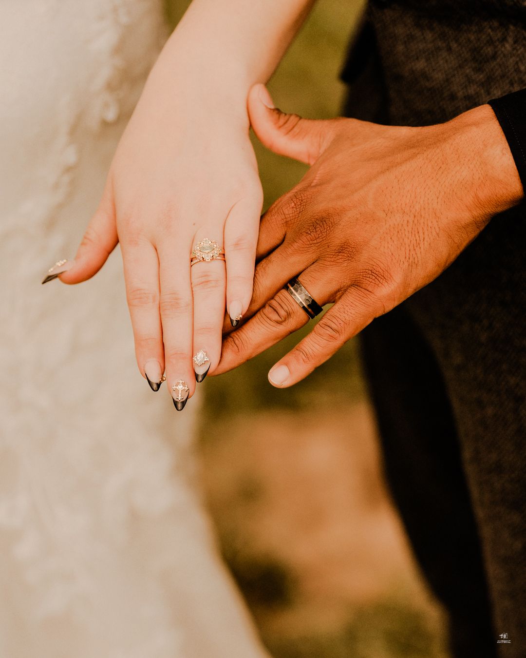 Close-up of newlyweds hands showing wedding rings, bride with black French tip nails and gold engagement ring.