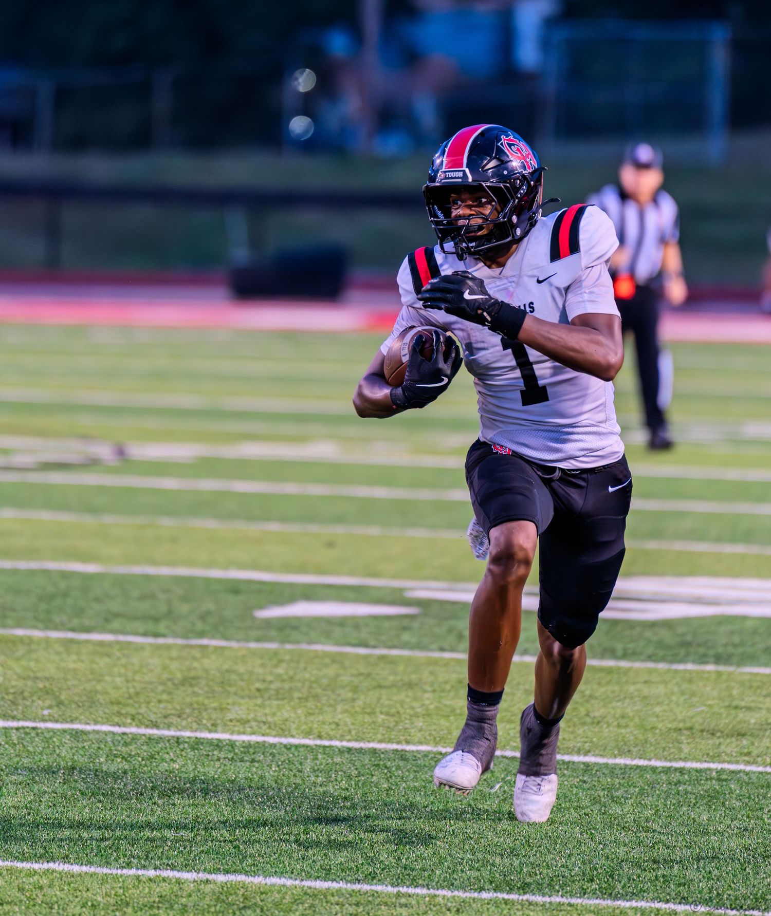 Football player #1 in black uniform runs with the ball during a night game.