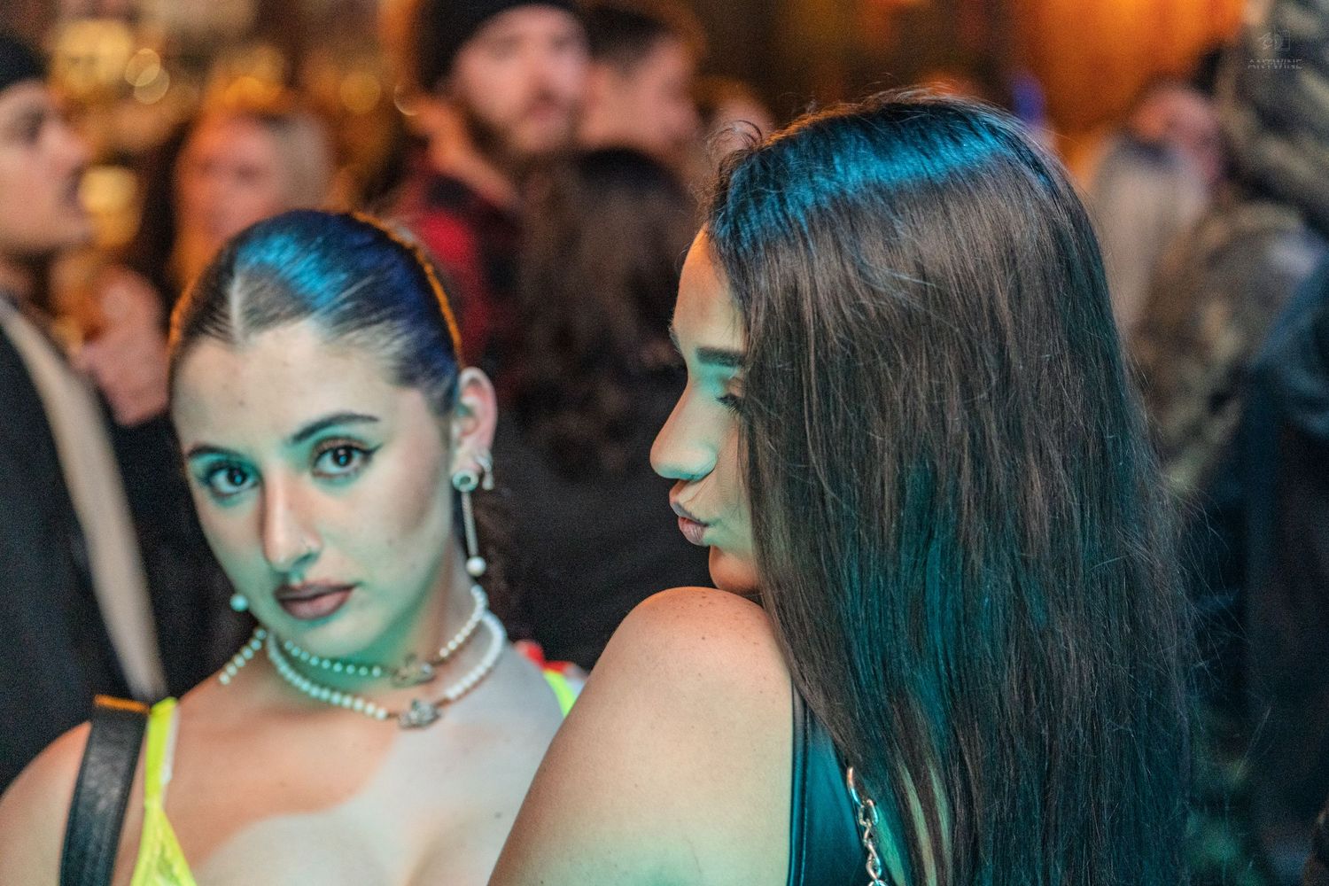 Two young women posing together under green and blue lights at a party.
