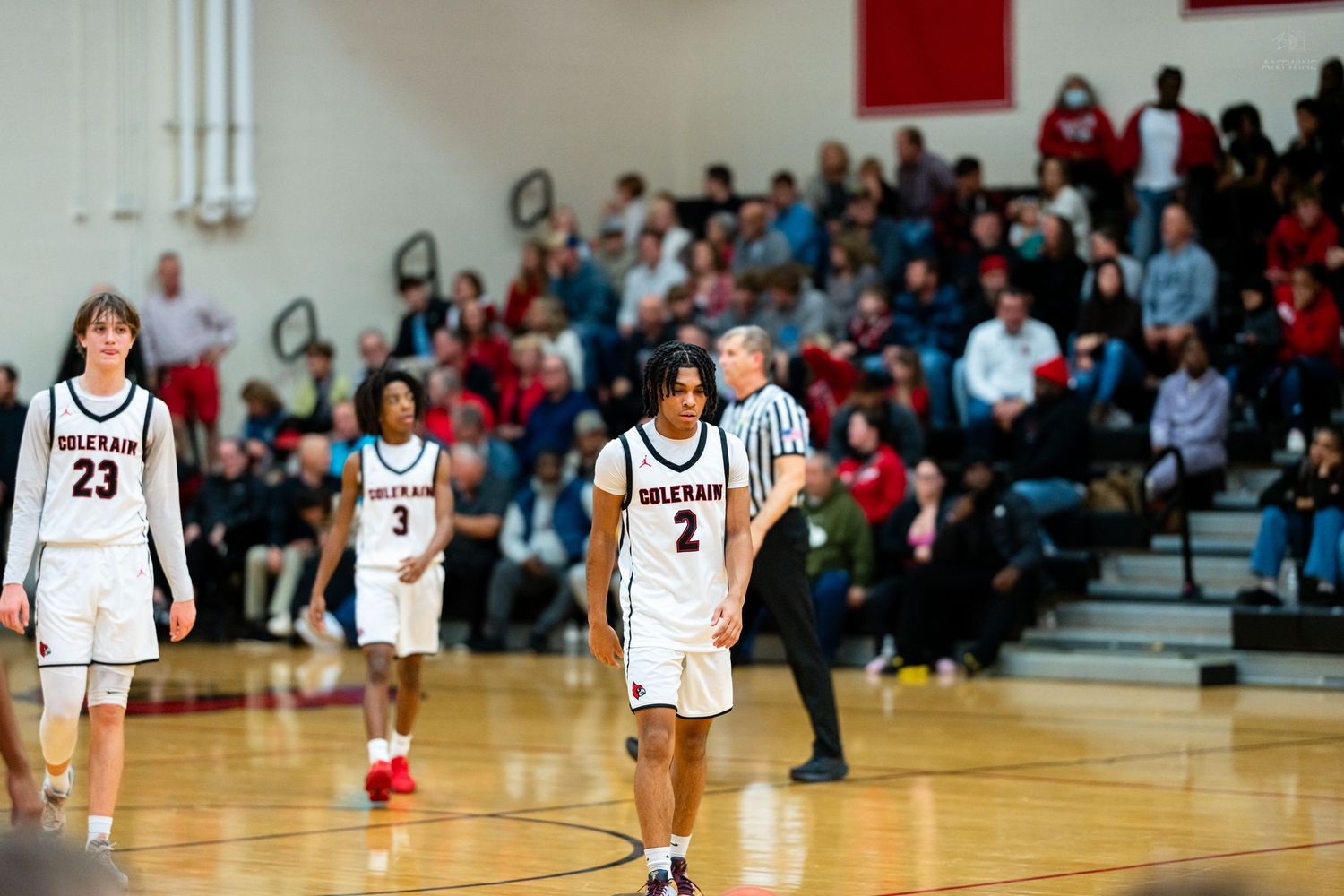 Three Cardinals basketball players walk across court during high school game with full crowd.