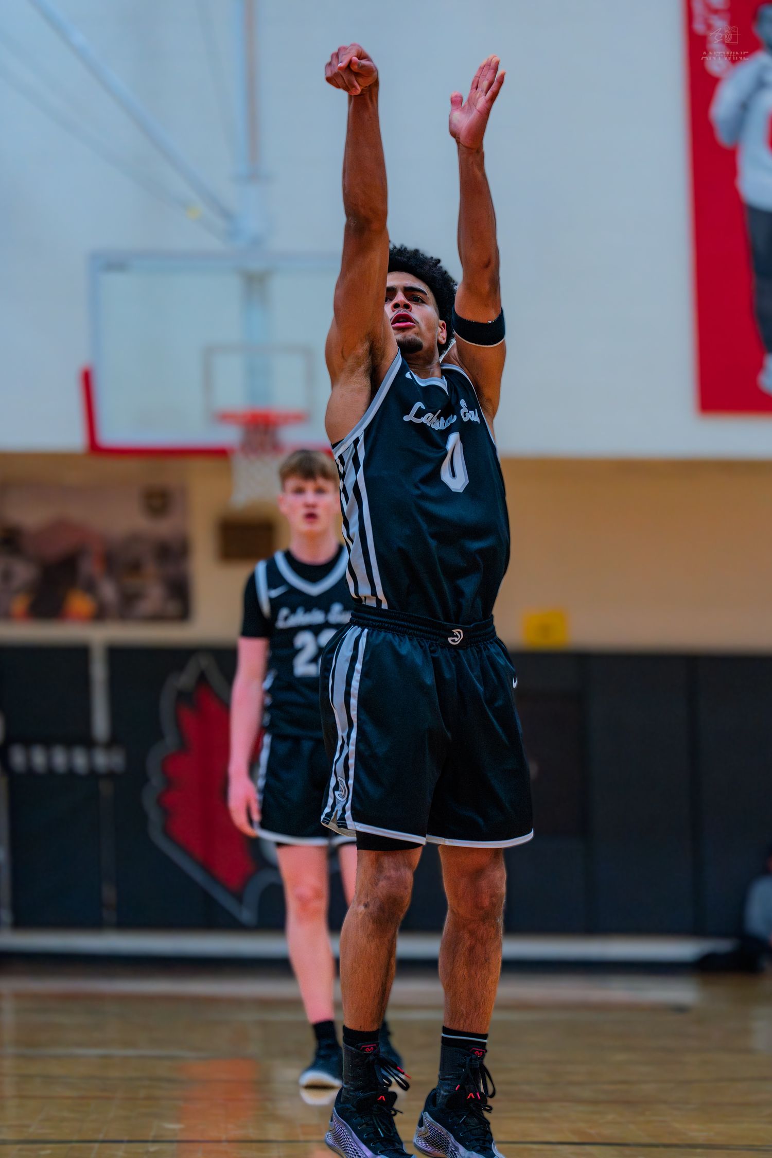 Lakota East basketball player #0 follows through on a jump shot with both arms raised during a game.