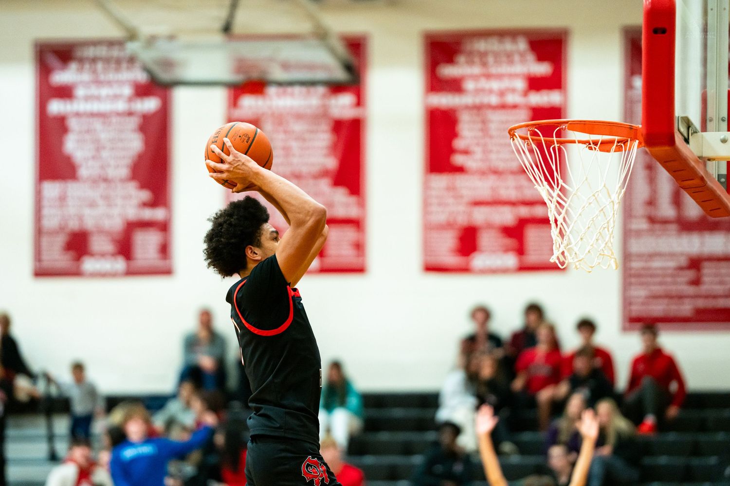 Athletic player rises for slam dunk in black uniform during high school basketball game.