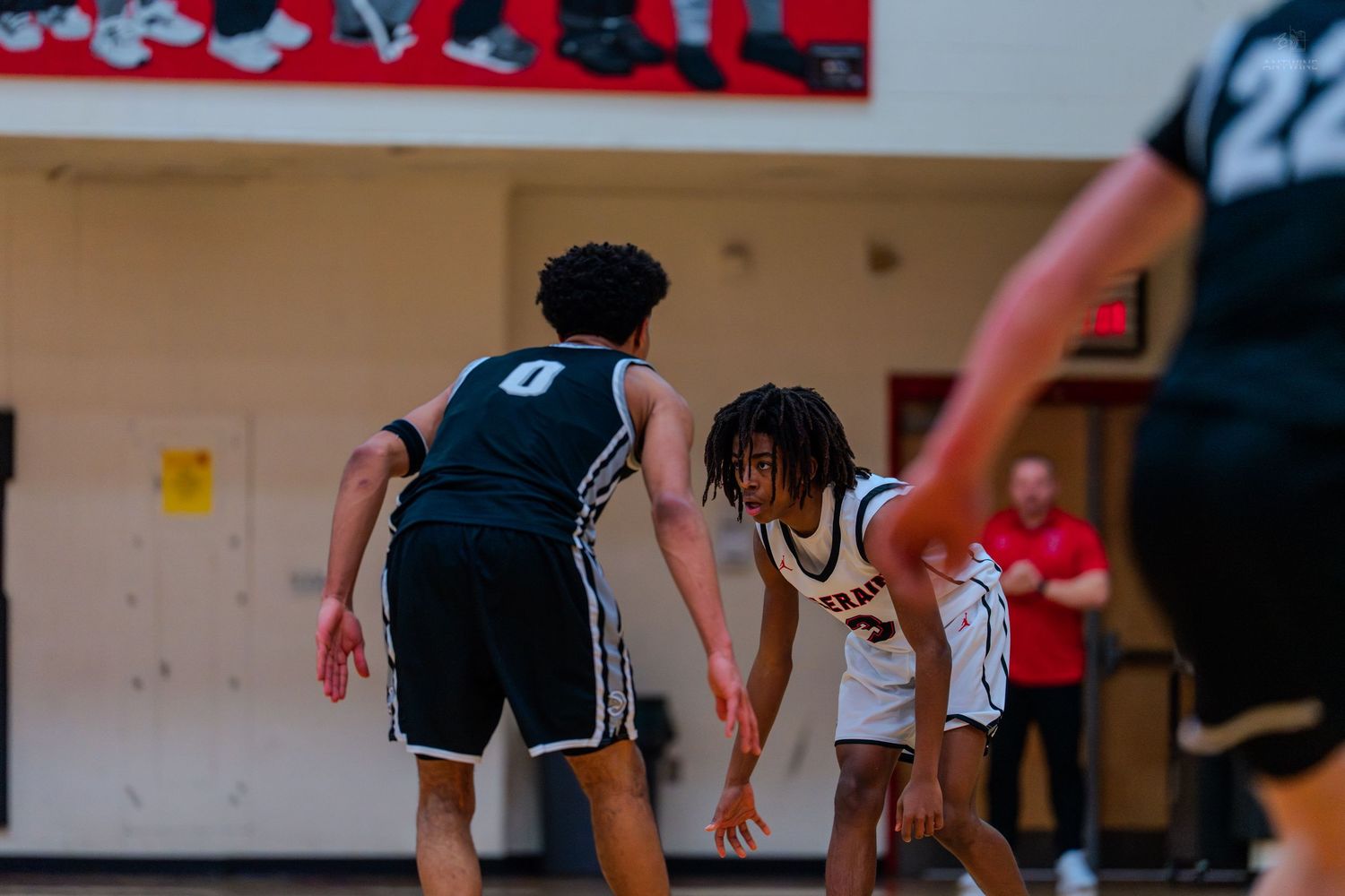 Two basketball players face off during a high school game, with player #0 in black defending against player #3 in white.