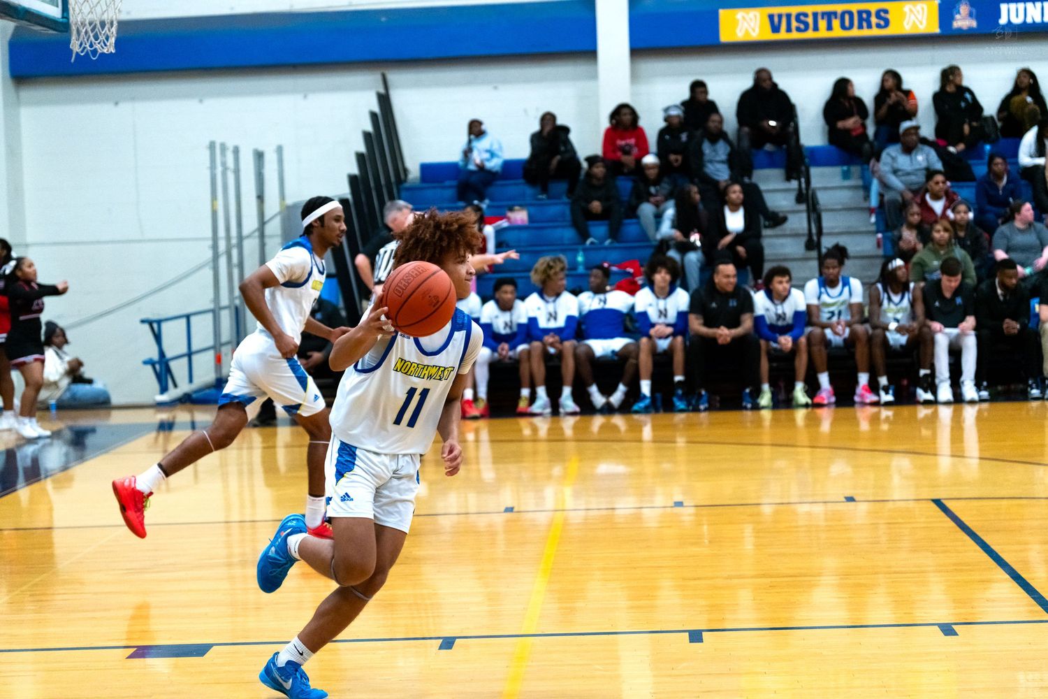 Player #11 in blue and yellow uniform dribbles ball downcourt during high school basketball game.