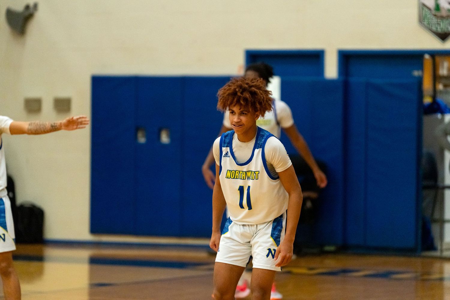 High school basketball player #11 in white and blue uniform stands alert on the court during a game.