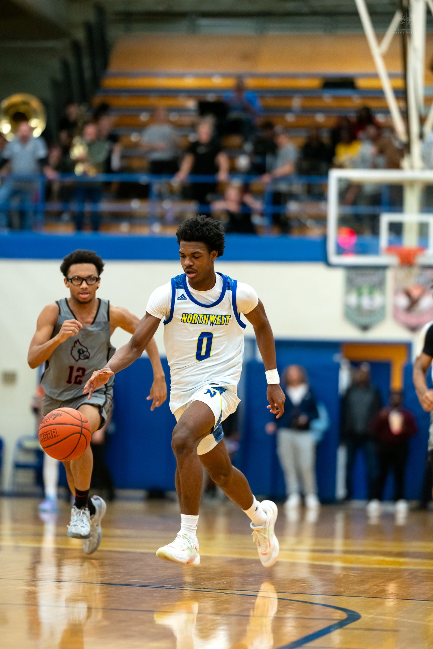 High school basketball player wearing number 0 dribbles upcourt during a competitive indoor game.