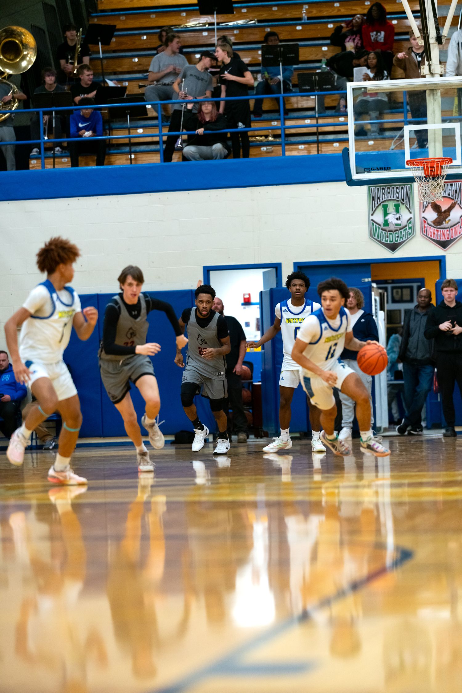 Blue and white team players drive fast break down court during high school basketball game.