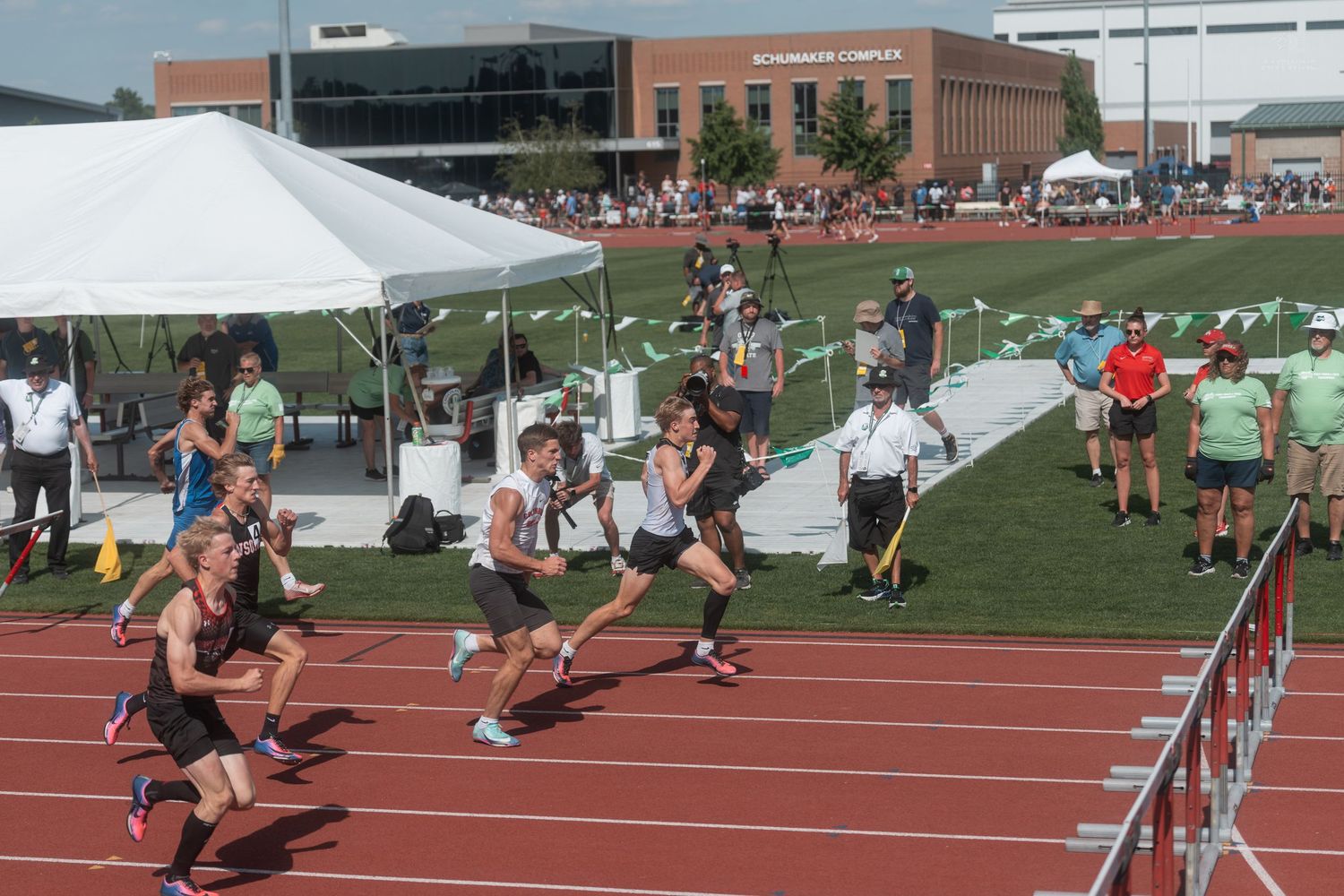 Relay race runners exchanging batons on red track at outdoor high school track and field championship event.