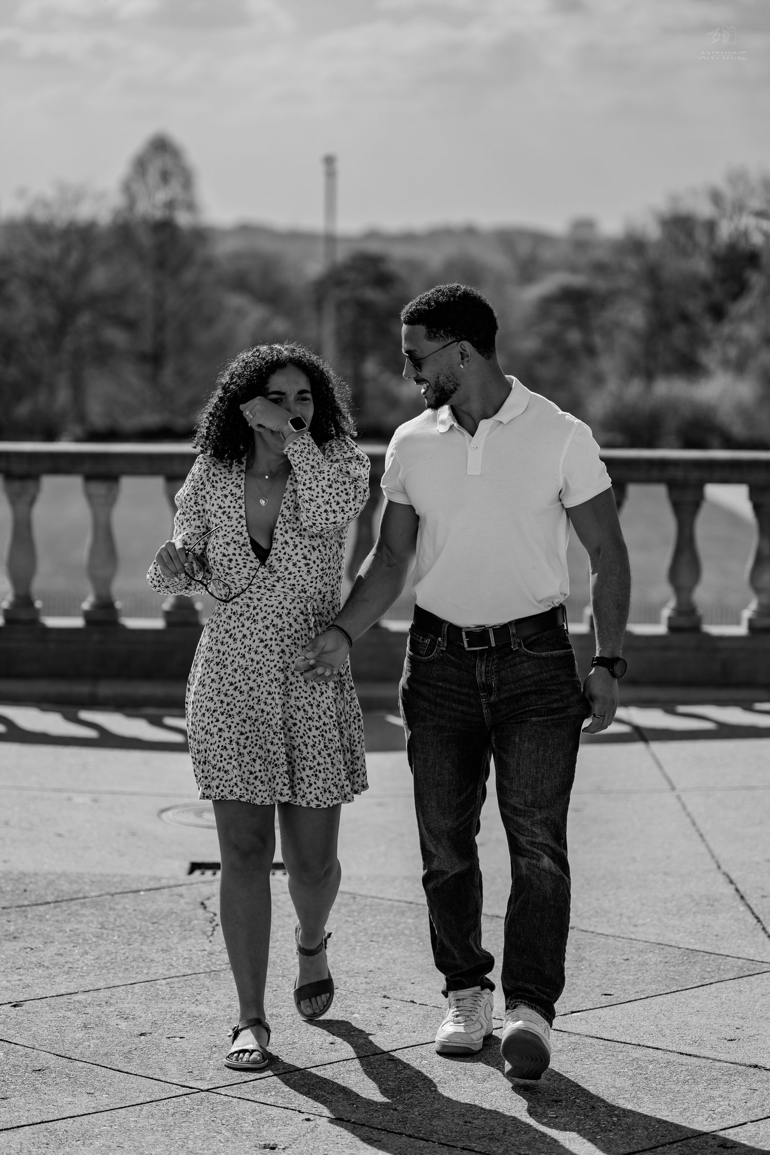 Black and white photo of a couple walking together on a terrace, smiling at each other on a sunny day.