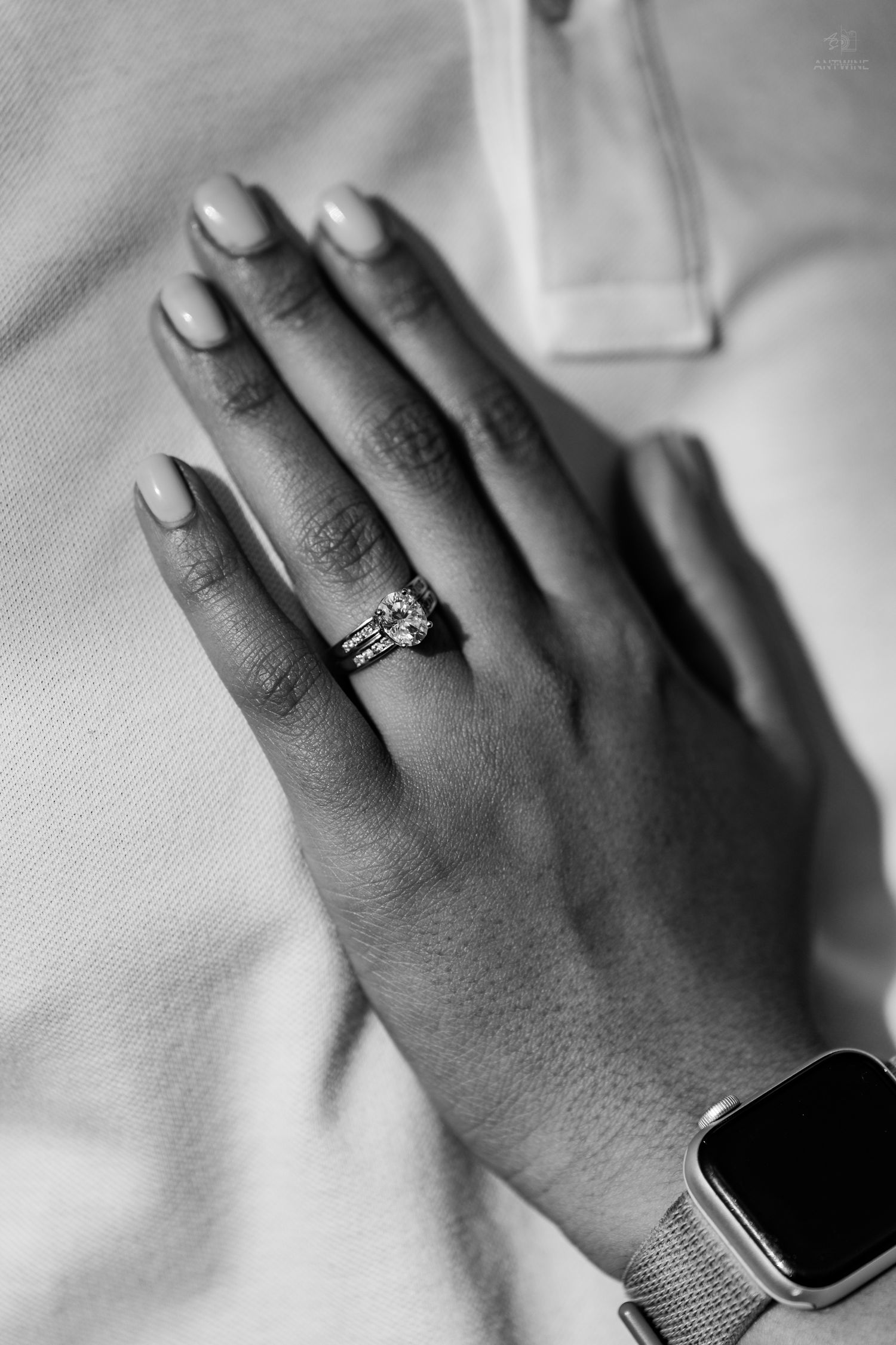Black and white close-up of a womans hand wearing a stunning diamond engagement ring with gold band.