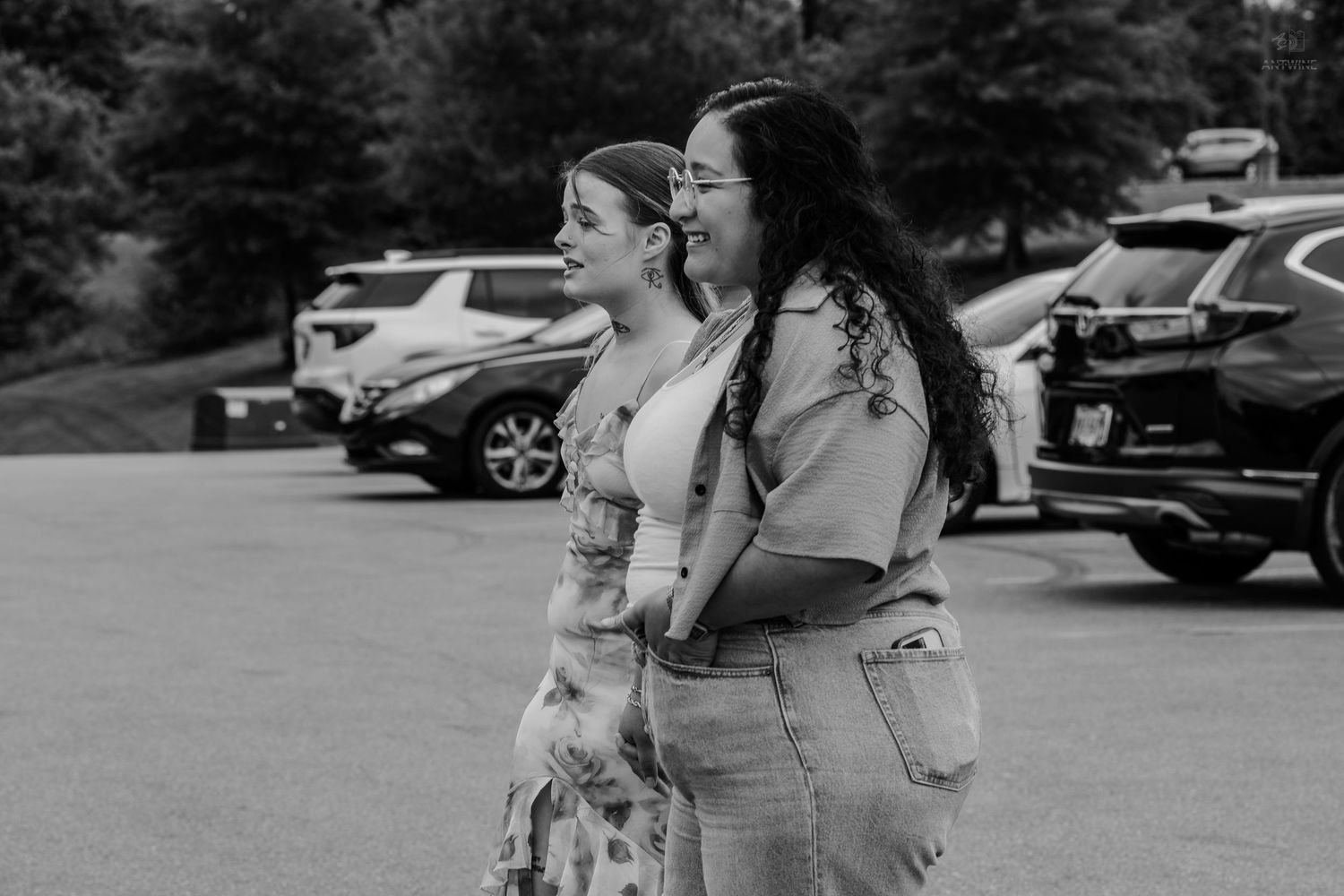 Black and white photo of two women walking and laughing together in an outdoor parking lot.