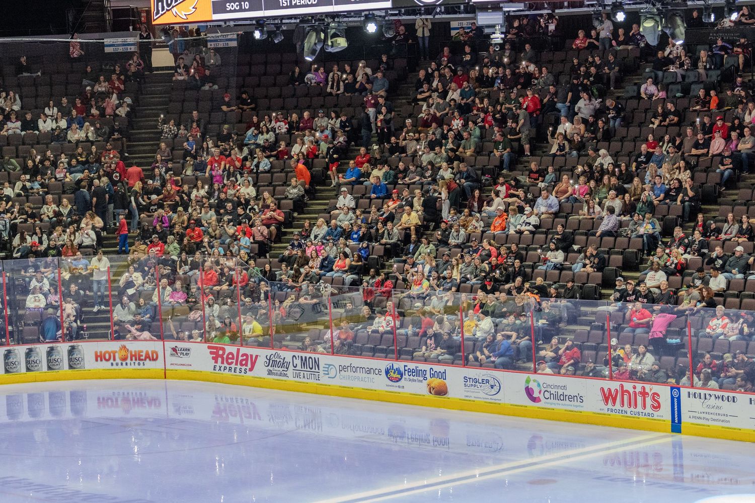 A large crowd of hockey fans fills the arena stands watching a game from behind the glass barrier.