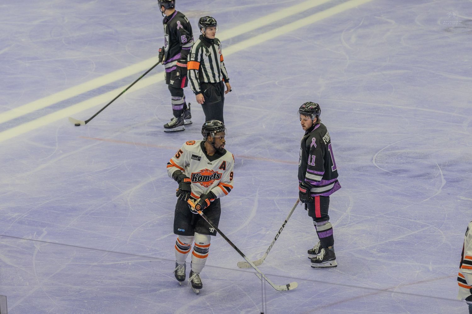 Two ice hockey players from opposing teams skate near center ice during a game.