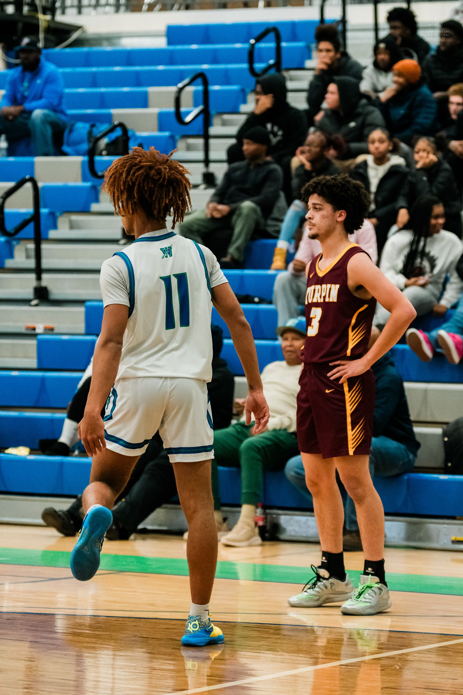 Turpin #3 basketball player stands courtside watching Warriors #11 dribble during high school game.